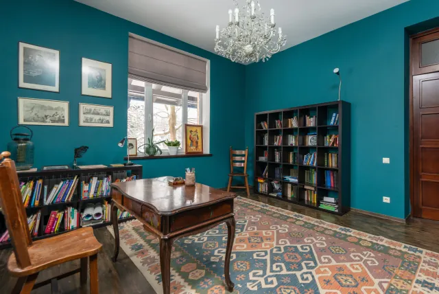 Patterned kilim in orange, blue and cream on the floor of a teal study