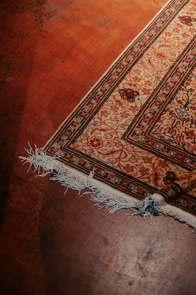 Corner of a red and ivory hand-knotted Persian rug with fringe on a dark wood floor