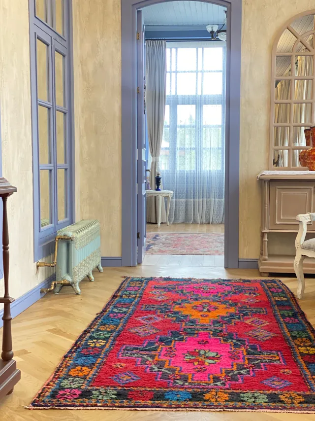 Vintage rug in magenta, red and orange on a herringbone floor in a hallway