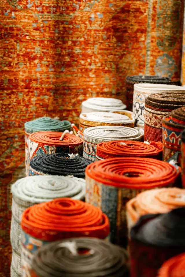 Rolled rugs in orange, grey and blue standing in front of a rust colored rug